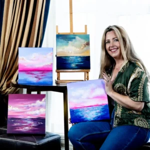 Orla Hickey sitting with her seascape paintings surrounding her